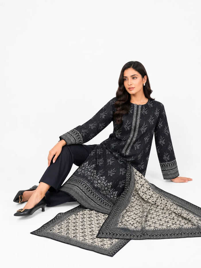 A woman models a three-piece black and gray printed ethnic suit consisting of a long-sleeve kurta, matching trousers, and a patterned dupatta against a plain white studio background.