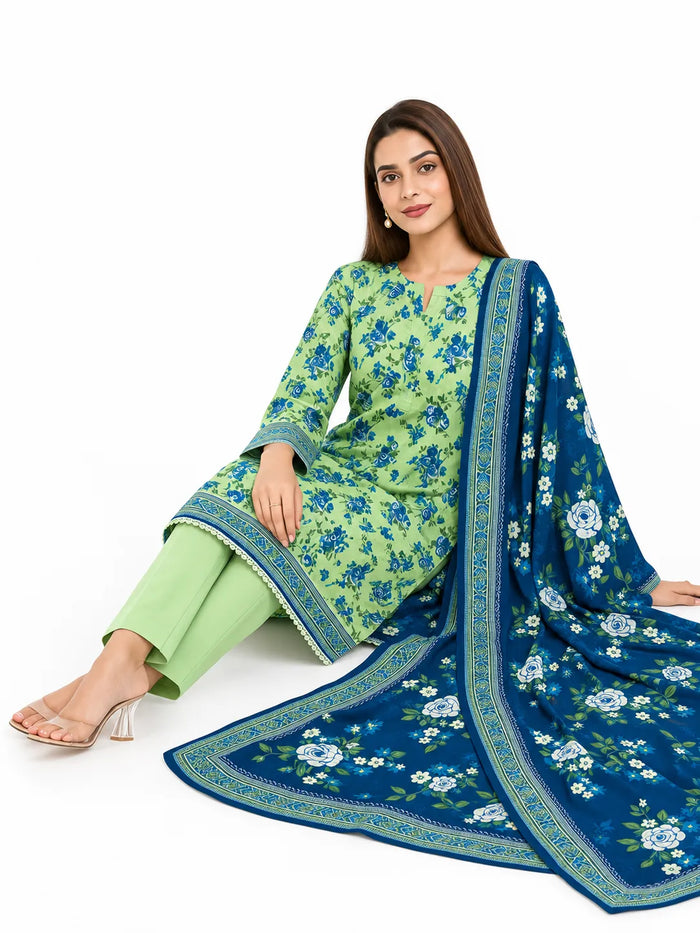 A woman models a three-piece Indian salwar kameez suit set. The set includes a light green kurta with blue floral prints and border detailing, matching light green trousers, and a navy blue dupatta with white floral prints and a gold border.