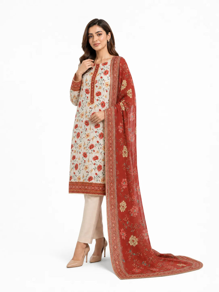 A woman models a traditional South Asian salwar kameez suit set. The set features a cream-colored kurta with red and green floral prints, beige trousers, and a rust-red dupatta with gold floral motifs and borders.